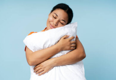 1 Happy African American woman sleeping, holding white pillow isolated on blue background. Morning concept